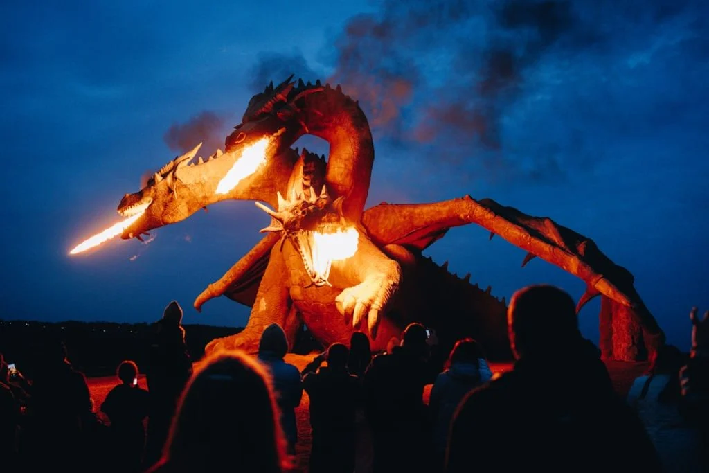 A massive dragon sculpture breathes fire over a crowd at dusk, capturing the epic dragon warfare spectacle of House of the Dragon Season 3